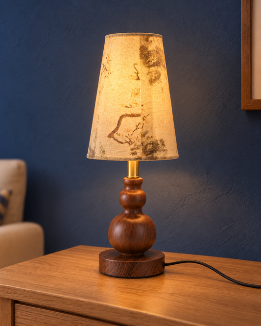 Spindle compact table lamp illuminated through its tall tapered patterned fabric shade