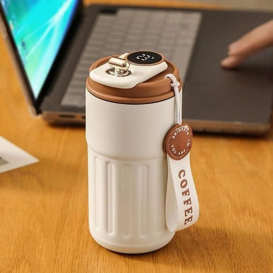 Beige travel mug with brown lid and 'COFFEE' strap on a wooden desk with a laptop.